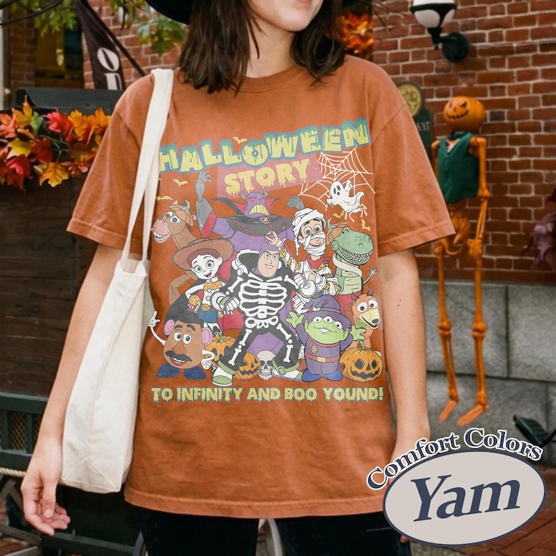 May include: Orange Comfort Colors t-shirt with a Halloween graphic featuring cartoon characters and the text "HALLOWEEN STORY" and "TO INFINITY AND BOO YOUND!". The shirt has a crew neck and short sleeves.