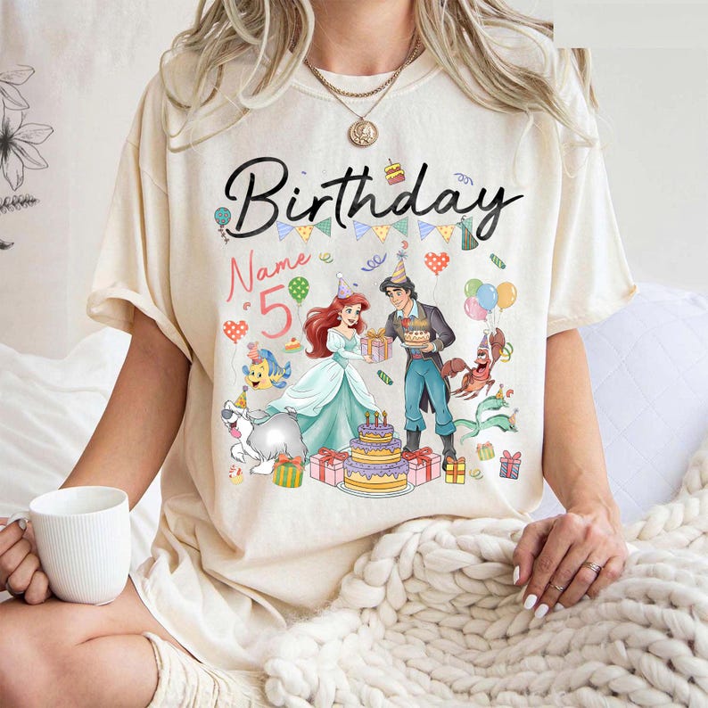 Pode incluir: Camiseta creme com um gr&aacute;fico de anivers&aacute;rio colorido. O design apresenta a palavra "Birthday" em escrita preta, o n&uacute;mero "5" e personagens de desenhos animados. A camiseta tem mangas curtas e um corte folgado.