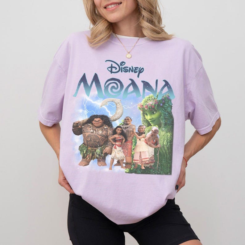 Pu&ograve; includere: T-shirt lilla chiaro con grafica del film Disney "Moana". La grafica include il titolo del film, i personaggi e un fulmine. La maglietta &egrave; a girocollo.