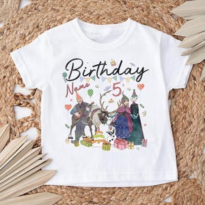 May include: White t-shirt with a colorful graphic featuring the text "Birthday" and "5". The design includes cartoon characters, a reindeer, a birthday cake, and gift boxes, perfect for a child's birthday celebration.