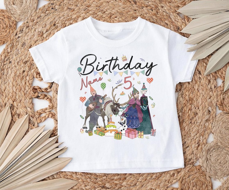 May include: White t-shirt with a colorful graphic featuring the text "Birthday" and "5". The design includes cartoon characters, a reindeer, a birthday cake, and gift boxes, perfect for a child's birthday celebration.