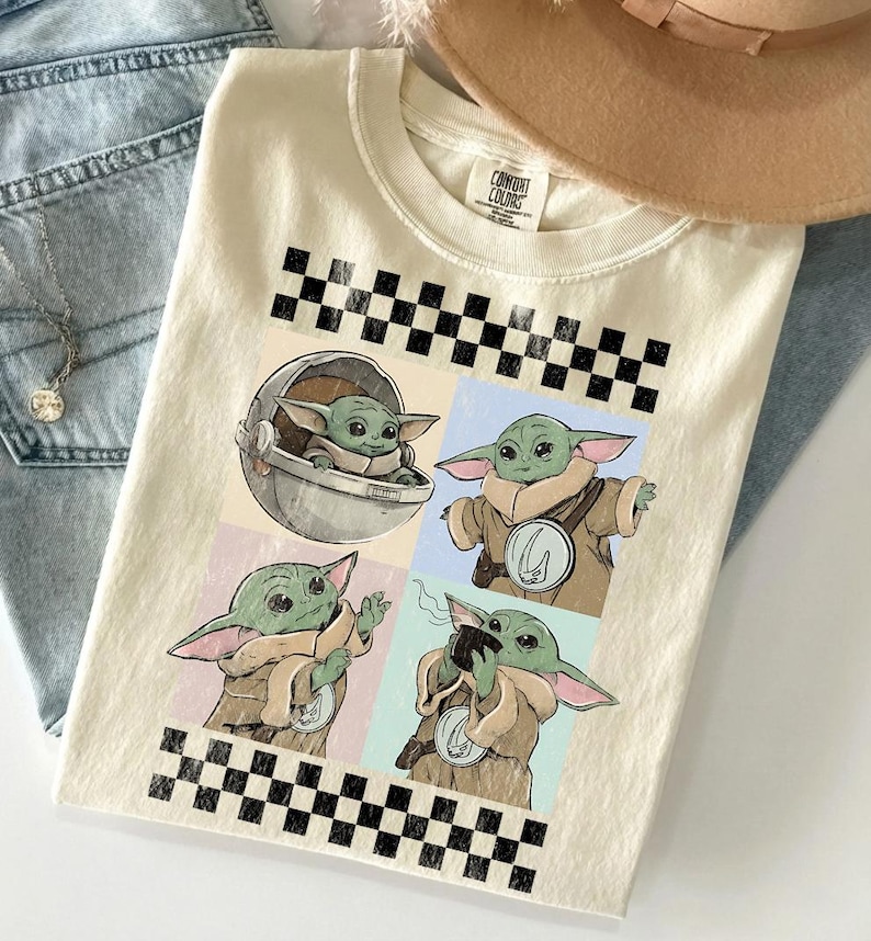 Puede incluir: Camiseta color crema con un gr&aacute;fico de cuatro paneles de un personaje alien&iacute;gena verde en varias poses. El dise&ntilde;o incluye un patr&oacute;n de tablero de ajedrez en blanco y negro y las palabras "COMFORT COLORS" en la etiqueta.