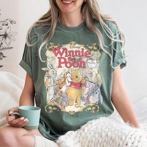 May include: Green t-shirt featuring a vintage-style graphic of Winnie the Pooh and friends. The design includes the text "Disney Winnie the Pooh" in a decorative frame, with characters like Pooh, Piglet, Tigger, and Eeyore.