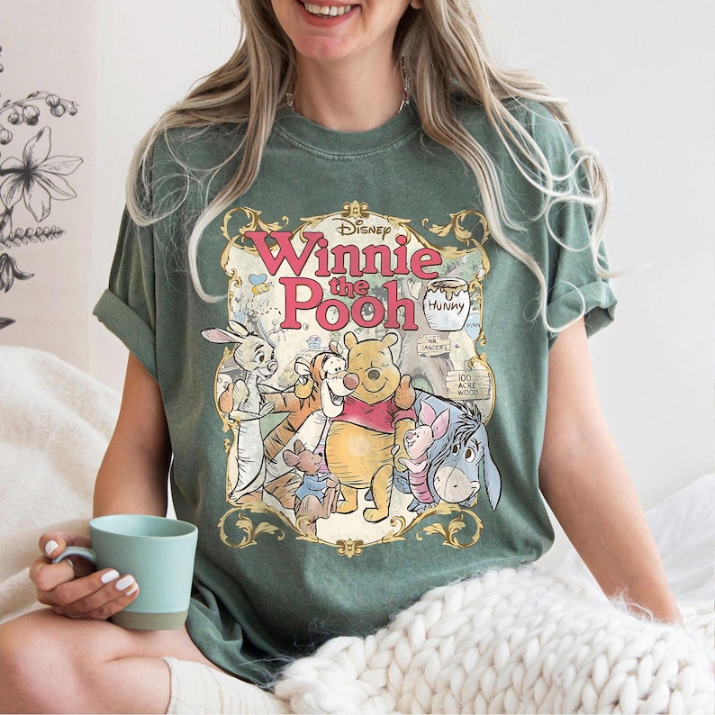 May include: Green t-shirt featuring a vintage-style graphic of Winnie the Pooh and friends. The design includes the text "Disney Winnie the Pooh" in a decorative frame, with characters like Pooh, Piglet, Tigger, and Eeyore.