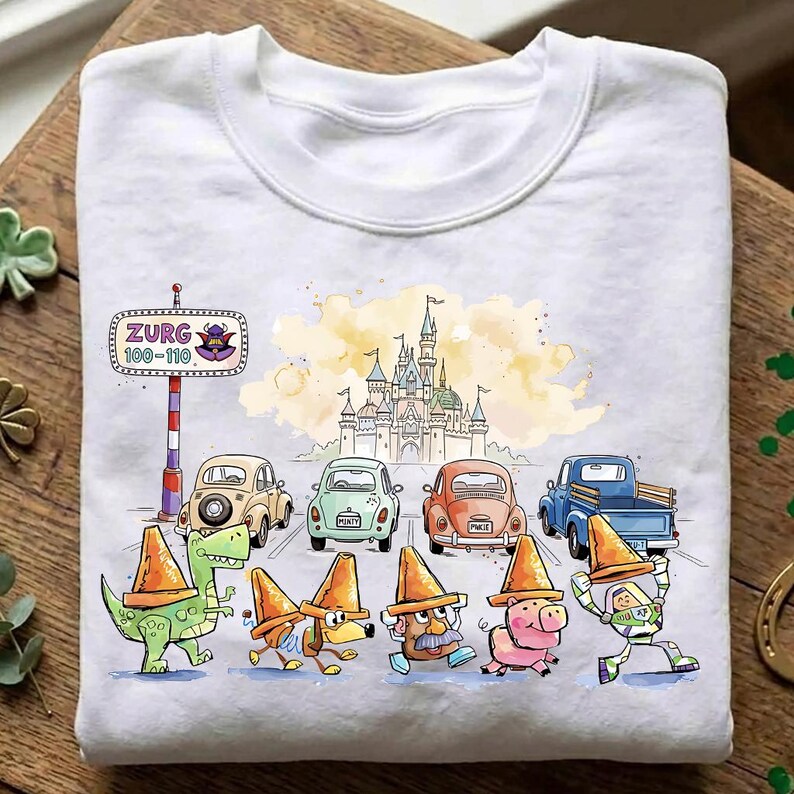 May include: White sweatshirt featuring a colorful cartoon design. The design includes a castle, cars, and characters wearing orange traffic cones. The text "ZURG 100-110" is also visible. The overall theme is playful and whimsical.
