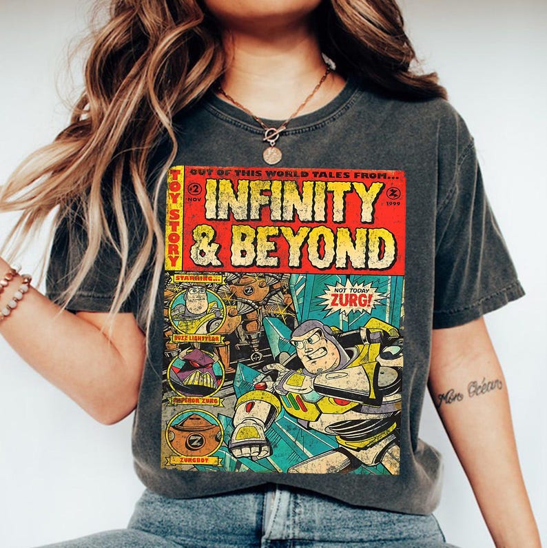 Może przedstawiać: Ciemnoszara koszulka z grafiką w stylu komiksu. Grafika przedstawia napis "INFINITY & BEYOND" oraz wizerunki Buzza Astrala i Zurga. Koszulka ma wygląd vintage.
