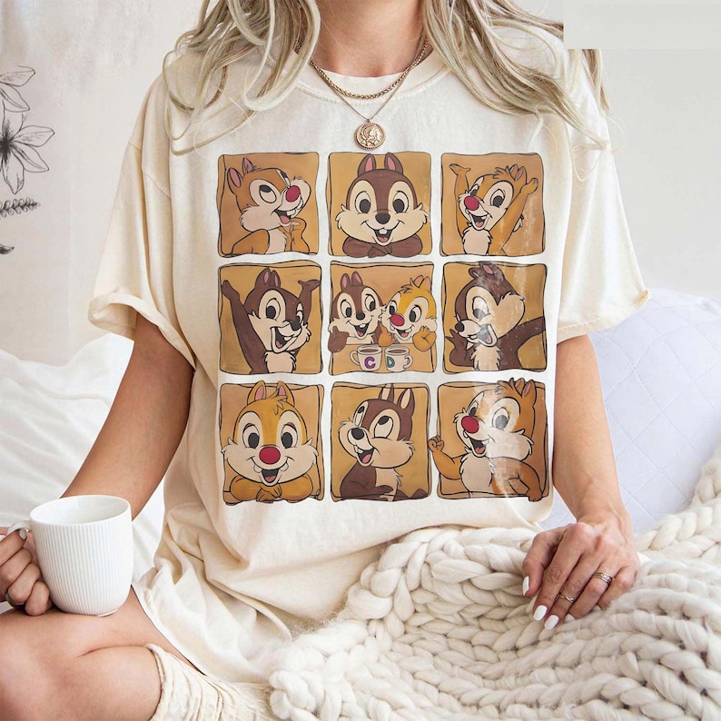 May include: Cream-colored t-shirt featuring a grid of nine cartoon chipmunks in various poses. The chipmunks are in brown squares with a light brown background. The shirt has short sleeves and a relaxed fit.