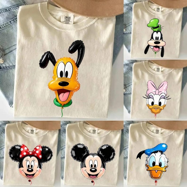May include: A collection of cream-coloured crew neck t-shirts, each featuring a different Disney character depicted as a shiny, inflated balloon. The characters include Pluto, Goofy, Daisy Duck, Minnie Mouse, Mickey Mouse, and Donald Duck.