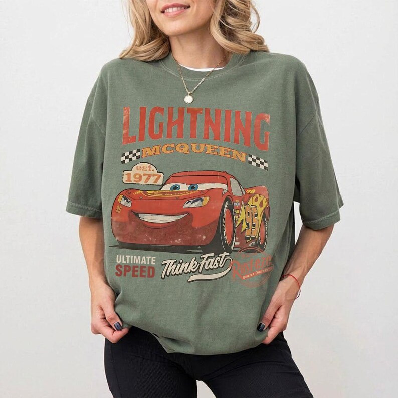 Puede incluir: Camiseta verde con Lightning McQueen de la pel&iacute;cula Cars. El dise&ntilde;o incluye el texto "LIGHTNING MCQUEEN" en naranja, el a&ntilde;o "1977" y las frases "ULTIMATE SPEED" y "Think Fast". El gr&aacute;fico es de estilo vintage.