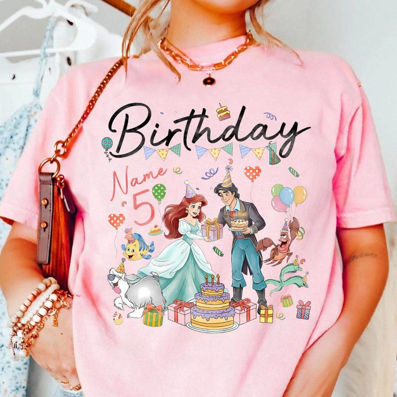 Pode incluir: Camiseta rosa com um gr&aacute;fico colorido de anivers&aacute;rio. O design inclui a palavra "Birthday", o n&uacute;mero "5", personagens de desenhos animados, um bolo, bal&otilde;es e caixas de presente.