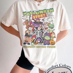 May include: Ivory t-shirt with a Halloween-themed graphic featuring characters and the text "HALLOWEEN STORY" and "TO INFINITY AND BOO YOUND!". The shirt is from Comfort Colors.