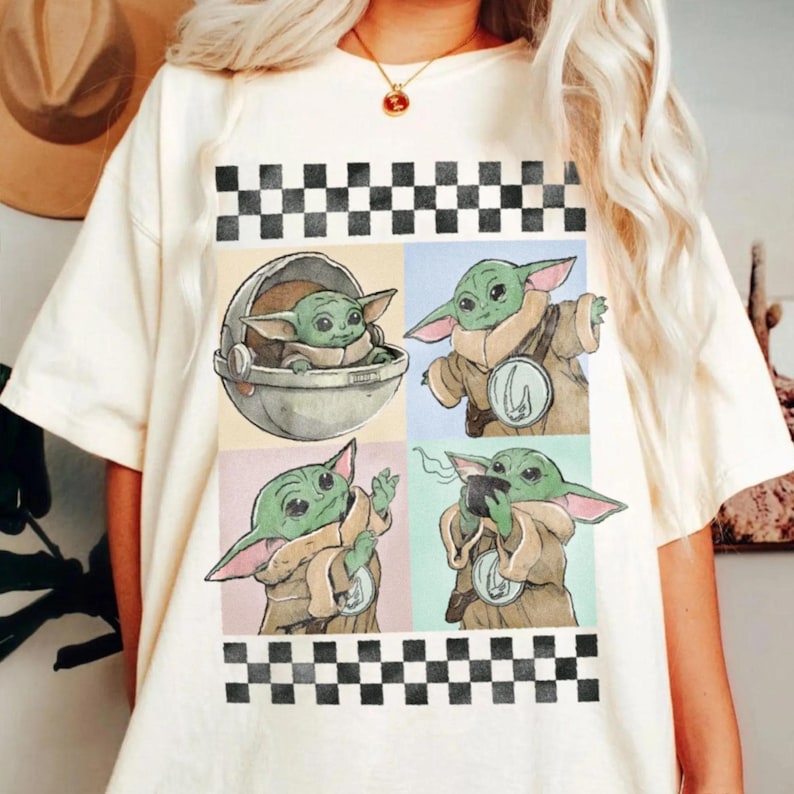 Puede incluir: Camiseta color crema con un gr&aacute;fico de cuatro paneles de un personaje alien&iacute;gena verde. El personaje se representa en varias poses, incluso en una c&aacute;psula, con una capa y sosteniendo una taza. Patr&oacute;n de cuadros blancos y negros en la parte superior e inferior.
