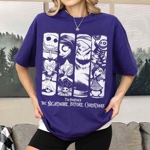 May include: A purple short-sleeved t-shirt featuring a white graphic print of characters from Tim Burton's The Nightmare Before Christmas. The design consists of four vertical panels displaying Jack Skellington, Sally, Oogie Boogie, and other figures.