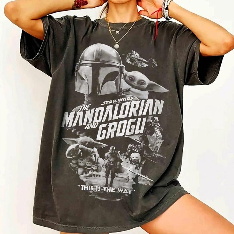 Peut inclure: T-shirt gris fonc&eacute; avec un graphisme de la s&eacute;rie Star Wars, "The Mandalorian and Grogu". Le design comprend le casque du Mandalorien, Grogu et la phrase "This is the Way".