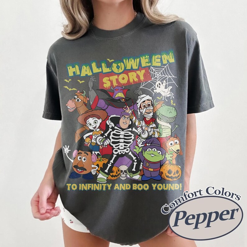 May include: Dark grey t-shirt with a colourful graphic of cartoon characters in Halloween costumes. The text "HALLOWEEN STORY" is at the top, with "TO INFINITY AND BOO YOUND!" below. The shirt has a Comfort Colors Pepper label.