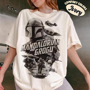 Peut inclure: T-shirt ivoire avec un graphisme de "The Mandalorian" avec le texte "The Mandalorian and Grogu" et "This is the Way". Le t-shirt porte &eacute;galement le texte "Comfort Colors" et "Ivory" dans un ovale.