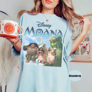 Pu&ograve; includere: T-shirt azzurra con il film Disney "Moana", personaggi e il titolo del film. La maglietta ha un girocollo e maniche corte. La parola "Chambray" &egrave; stampata in basso a destra sulla maglietta.