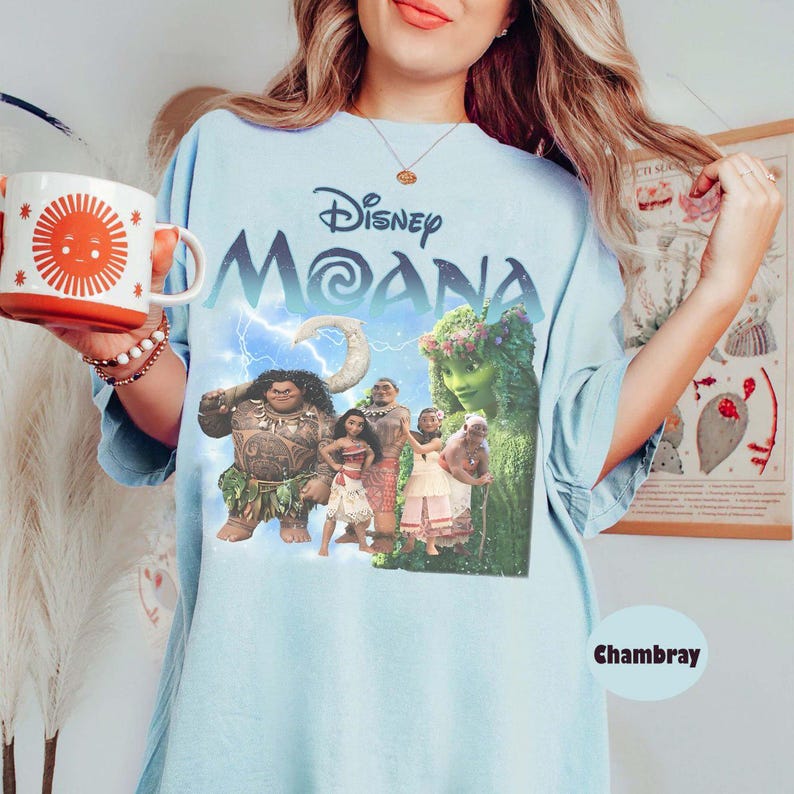 Pu&ograve; includere: T-shirt azzurra con il film Disney "Moana", personaggi e il titolo del film. La maglietta ha un girocollo e maniche corte. La parola "Chambray" &egrave; stampata in basso a destra sulla maglietta.