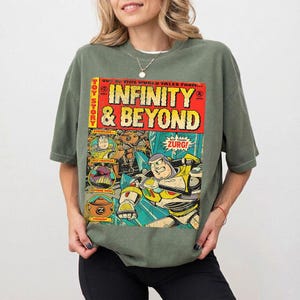 Może przedstawiać: Zielona koszulka w kolorze oliwkowym z komiksową grafiką z Toy Story. Grafika przedstawia "INFINITY & BEYOND" pogrubioną czcionką, wraz z obrazami Buzza Astrala i Zurga. Koszulka ma kr&oacute;tkie rękawy i luźny kr&oacute;j.