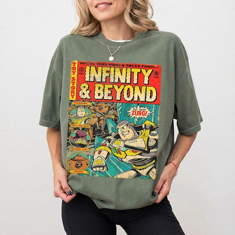 Może przedstawiać: Zielona koszulka w kolorze oliwkowym z komiksową grafiką z Toy Story. Grafika przedstawia "INFINITY & BEYOND" pogrubioną czcionką, wraz z obrazami Buzza Astrala i Zurga. Koszulka ma kr&oacute;tkie rękawy i luźny kr&oacute;j.