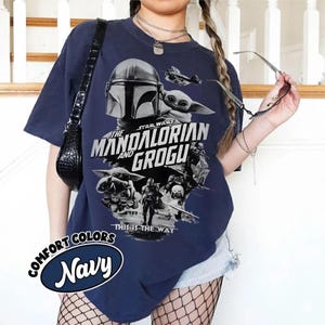 Peut inclure: T-shirt bleu marine avec un motif de The Mandalorian et Grogu de Star Wars. Le motif comprend le texte "The Mandalorian and Grogu" et "This is the Way". Le t-shirt porte &eacute;galement les mots "Comfort Colors" et "Navy" dans un design circulaire.