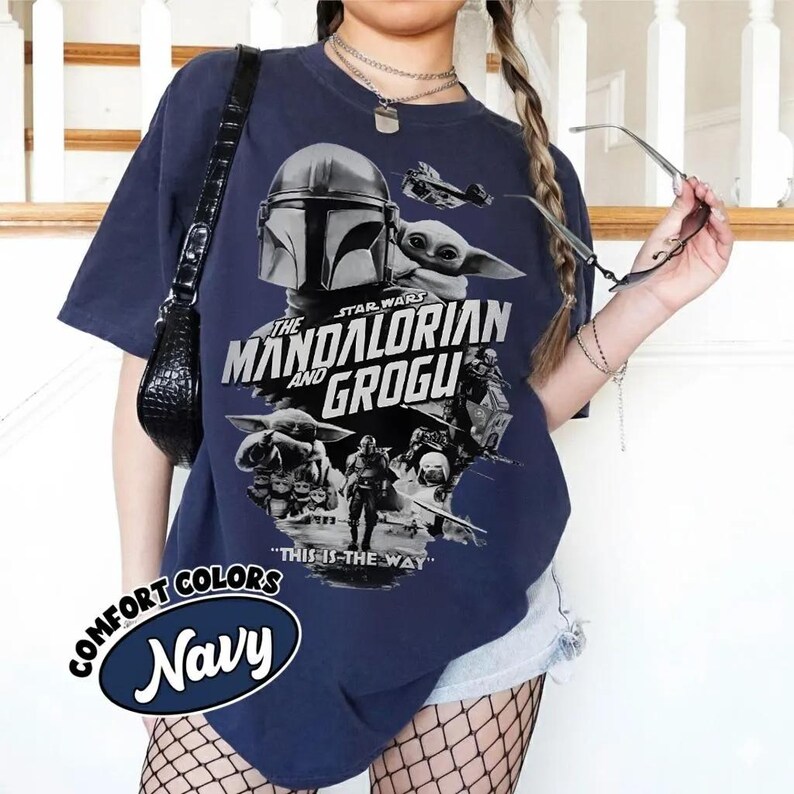 Peut inclure: T-shirt bleu marine avec un motif de The Mandalorian et Grogu de Star Wars. Le motif comprend le texte "The Mandalorian and Grogu" et "This is the Way". Le t-shirt porte &eacute;galement les mots "Comfort Colors" et "Navy" dans un design circulaire.