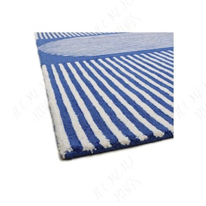 Könnte beinhalten: Blau-weiß gestreifter Teppich mit geometrischem Design. Der Teppich hat einen großen blauen Kreis und vertikale weiße Streifen auf blauem Hintergrund. Der Teppich besteht aus einem weichen, strukturierten Material.