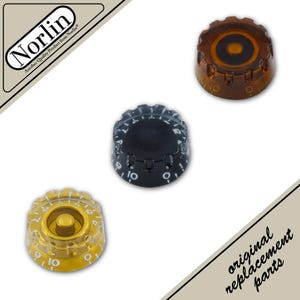 May include: Three circular guitar control knobs featuring a ridged edge and numbered scale from zero to ten. One knob is translucent amber, one is solid black, and one is gold with a clear outer shell. The Norlin logo is visible in the corner.