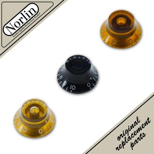 May include: Three bell-shaped guitar control knobs featuring numbered scales from zero to ten. Two knobs are translucent amber with gold-colored inserts, and one knob is solid black with white numbering. The Norlin logo and text are visible.