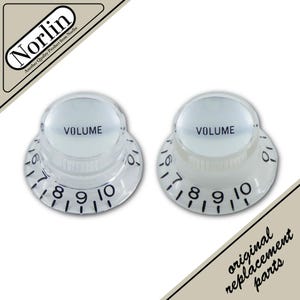 May include: Two clear plastic volume control knobs for musical instruments. Each knob features a smooth top with the word VOLUME printed in black, and a flared base with black numerical markings from 1 to 10 around the outer edge.