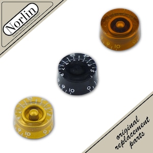 May include: Three circular control knobs for musical instruments, featuring numbered scales from 0 to 10. One knob is translucent amber, one is solid black with white numerals, and one is metallic gold with white numerals. Text Norlin appears.