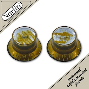 May include: Two amber-colored guitar control knobs with gold-tinted sides and silver-colored tops. Each knob features black numbering from 0 to 10 around the base. One knob is labeled TONE and the other VOLUME in black text on the silver top.