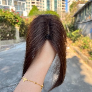 May include: A dark brown hair topper with a natural-looking part. The hairpiece appears to be made of human hair and is designed to add volume and coverage. The hair is long and straight.