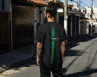 Op de afbeelding: Zwart t-shirt met een groen grafisch ontwerp op de achterkant. Het ontwerp bevat een verticale tekstregel en een kaartachtige vorm. De tekst op het shirt luidt "Rio de Janeiro" en "Cidade Maravilhosa".