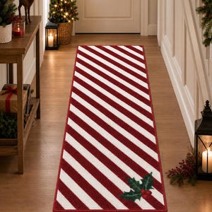 May include: A rectangular runner rug featuring a diagonal red and white striped pattern. The rug has a red border and a decorative holly leaf and berry graphic located in the bottom right corner. The design is consistent across the entire surface.