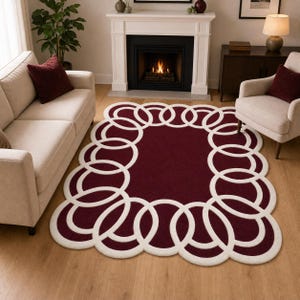 May include: A rectangular area rug featuring a deep burgundy centre and a thick, white, interlocking circular border pattern. The rug has a scalloped edge design created by the continuous white rings that frame the solid dark red interior field.