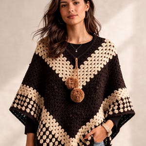 Könnte beinhalten: Ein handgefertigter Häkelponcho in einem geometrischen Muster. Der Poncho hat eine dunkelbraune und cremefarbene Farbgebung mit einem V-Ausschnitt. Zwei braune Pompons hängen vom Ausschnitt. Der Poncho ist ein stilvolles und gemütliches Kleidungsstück.