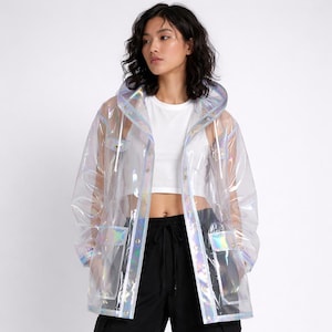 Könnte beinhalten: Ein klarer, schillernder Regenmantel mit Kapuze, Taschen und Knopfverschlüssen. Die Jacke hat einen holografischen Glanz, der mehrere Farben reflektiert. Das Model trägt ein weißes Oberteil und eine schwarze Hose. Ein stilvolles Oberbekleidungsstück.