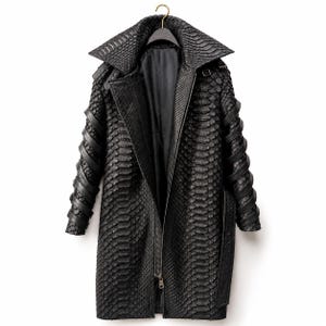 Peut inclure: Un manteau noir présentant un motif texturé en forme d'écailles sur l'extérieur. Le vêtement comprend un large col, une fermeture éclair centrale et des manches longues ornées de lanières noires en spirale entourant les bras.
