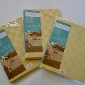 May include: Three spill-proof, microfiber tablecloths in a light yellow checkered pattern. Each tablecloth is packaged in clear plastic with a teal and white label that reads "Home Classics" and "Spill-Proof Microfiber Tablecloth".