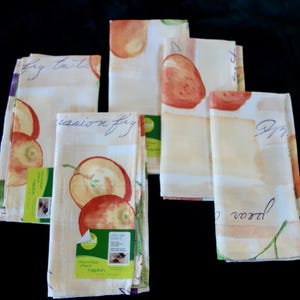Könnte beinhalten: Eine Sammlung von Mikrofasertüchern mit Obstmotiven. Die Servietten zeigen Aquarellillustrationen von Äpfeln und Birnen in Rot-, Orange- und Grüntönen. Der Text "mission fig" und "pear" ist sichtbar.