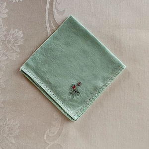 May include: A light green linen napkin with a small embroidered red rose design.