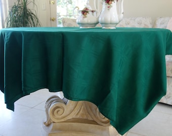 May include: A dark green tablecloth draped over a decorative table. The tablecloth has a subtle woven pattern. Two decorative ceramic pieces with floral designs sit on top of the table.