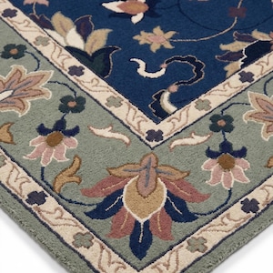 May include: Close-up of a corner of a blue and green floral patterned rug. The rug features a central blue field with floral motifs in shades of pink, beige, and brown. The border is green with a beige floral design.