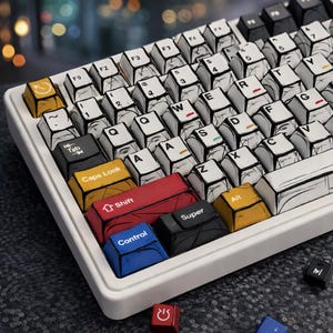 May include: A white mechanical keyboard with custom keycaps. The keycaps have a black and white comic book style design. The keyboard features keys in various colours, including red, yellow, blue, and black. The keyboard is on a dark grey surface.
