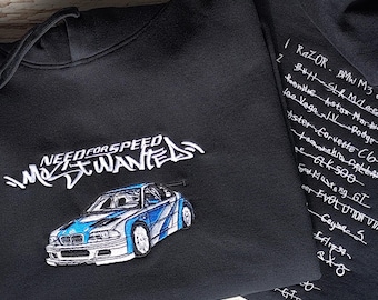 May include: A black hooded sweatshirt featuring an embroidered Need for Speed Most Wanted logo and a blue and white sports car. The back of the hoodie displays a list of embroidered car names and models in white thread, including Razor BMW M3 GTR.