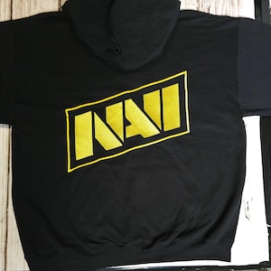 Puede incluir: Sudadera con capucha negra con un logotipo amarillo y negro en la espalda. El logotipo es un diseño estilizado con las letras NAI dentro de un rectángulo amarillo. La sudadera tiene capucha y mangas largas.