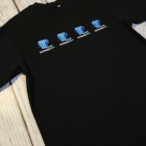 Puede incluir: Camiseta negra con una serie de gráficos estilizados de la letra "T" en azul y blanco, cada uno con el texto "Katowice 2014". La camiseta está hecha de un material suave.