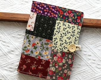Könnte beinhalten: Eine Patchwork-Stoff-Zeitschriftenhülle mit Knopfverschluss. Die Hülle besteht aus verschiedenen floralen und gemusterten Stoffen in Lila, Rot, Grün und Grau. Der Knopf hat eine hellbraune Farbe.