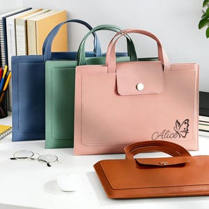 May include: Leather document holders in navy, green, pink, and brown. The pink bag features the name "Alice" and a butterfly design. Each has a handle and a front pocket. Ideal for carrying documents.